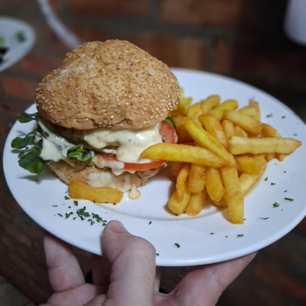Crispy chicken burger with fresh salad and golden chips on a white plate at My Hometown Café