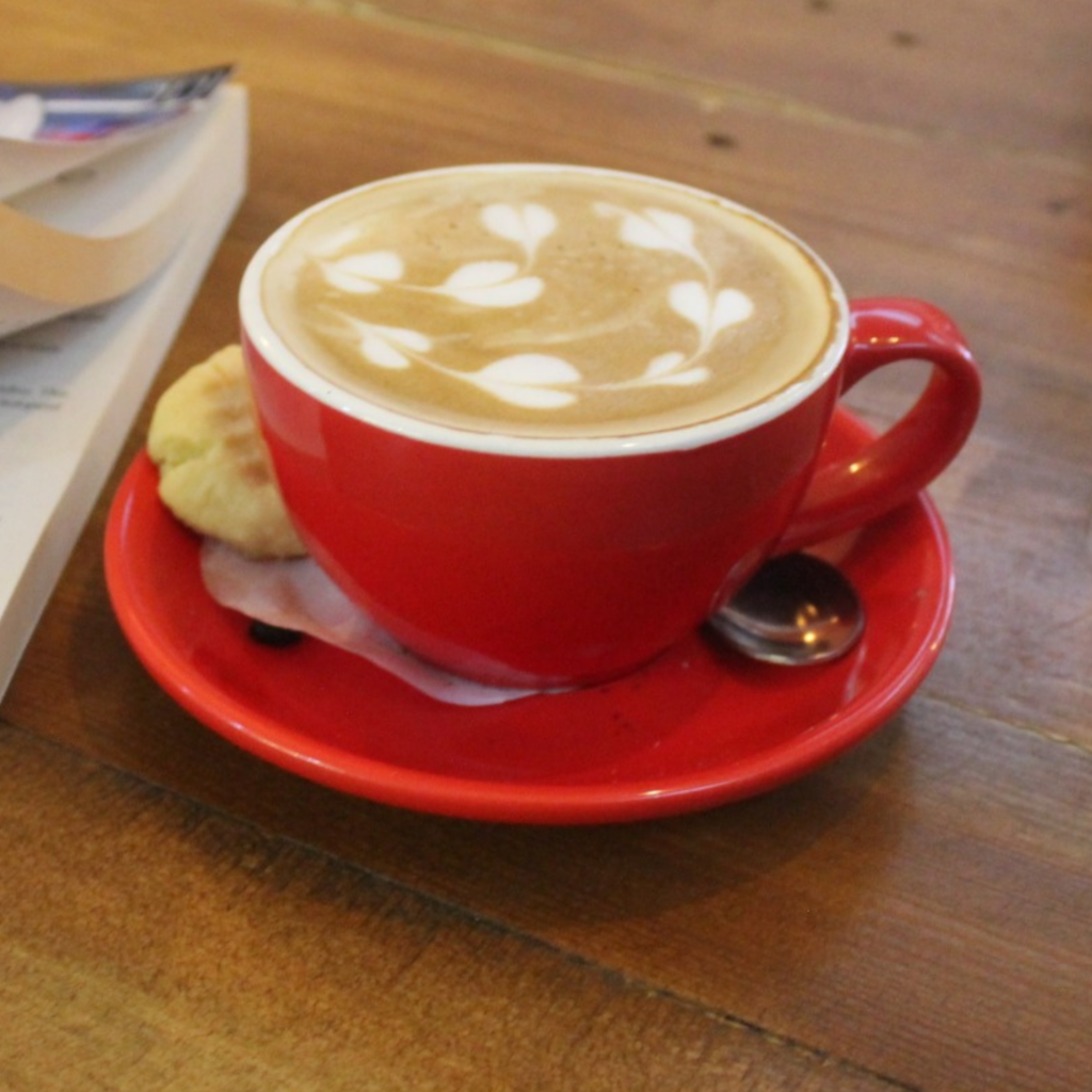 Creamy cappuccino with heart latte art in a red cup and saucer on a café table