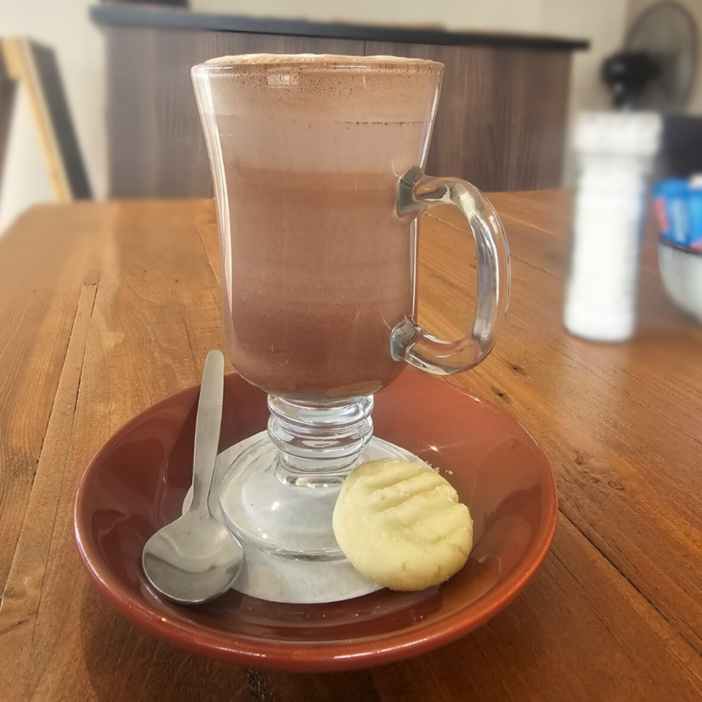 Rich hot chocolate with frothy top in a clear glass mug on a wooden café table
